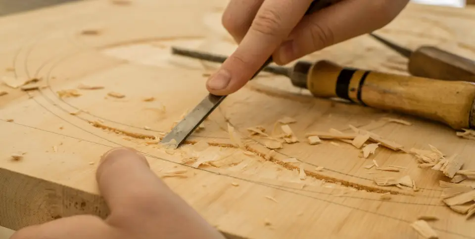 Hands carving a piece of wood with a chisel